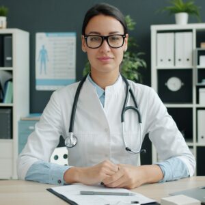 A female doctor wearing a stethoscope sits at her desk.